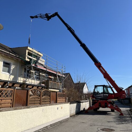 oter Kran hebt Baumaterial neben Wohnhaus für Zimmererarbeiten